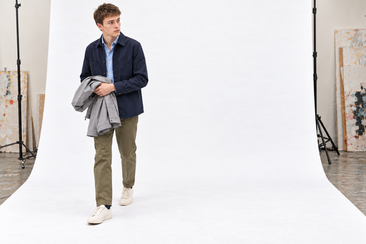 Practical first-visit outfit with a blue shirt, navy overshirt, olive chinos, cream trainers and a lightweight raincoat.