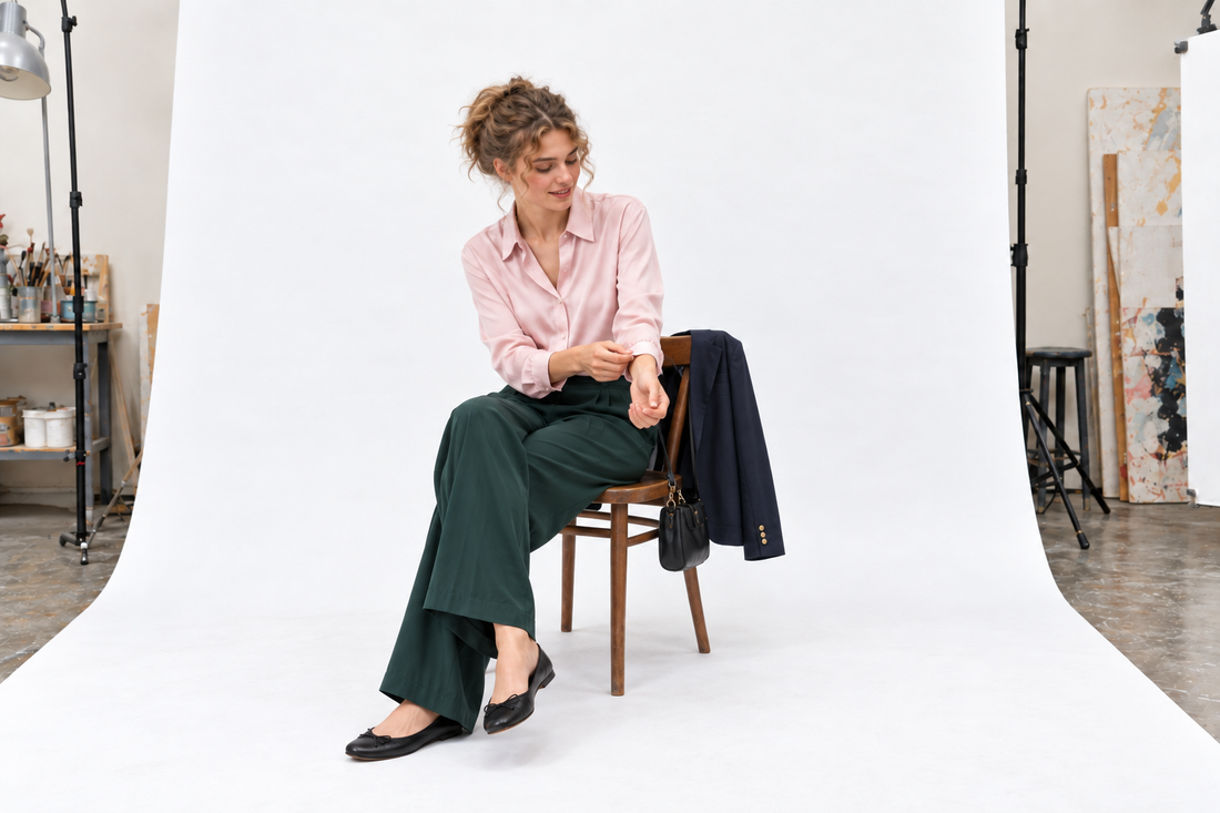 Woman adjusting a pale pink silk blouse cuff with deep green evening trousers and black flats.