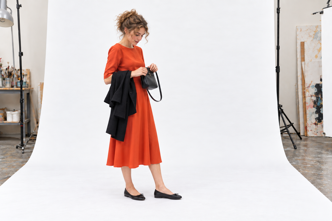 Woman checking a compact bag with an orange-red evening dress, black flats and a warm coat.