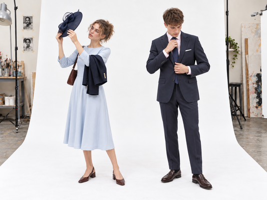 Woman checking a navy hat with a pale-blue dress beside a man adjusting his tie in a navy suit and pink shirt.