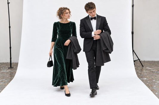 Woman in a bottle-green velvet evening dress and black flats beside a man in a black dinner suit, in the white studio.