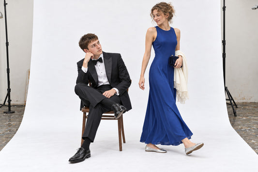 Woman in a cobalt evening dress and silver flats beside a man in a black dinner suit, in the white studio.