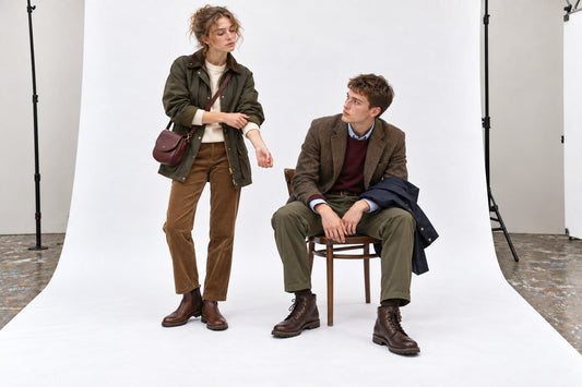 Woman in tobacco corduroy and an olive field jacket beside a man in tweed, burgundy knit and olive trousers.