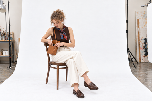 Woman in ivory trousers, a chocolate sleeveless knit and brown loafers, with a loosely tied silk neck scarf.